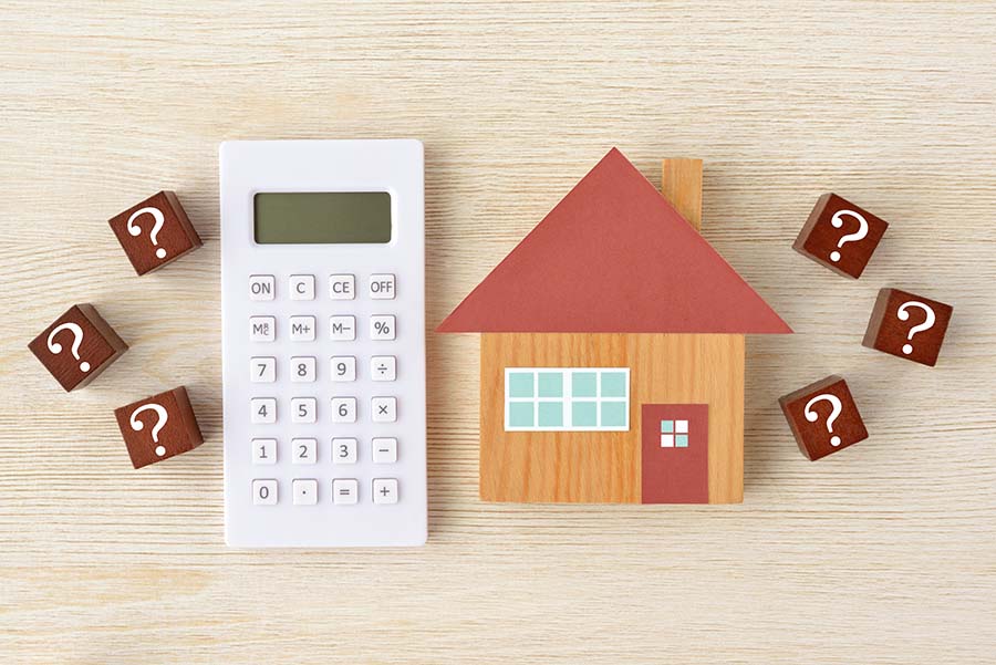 A small wooden house next to a calculator and surrounded by question marks