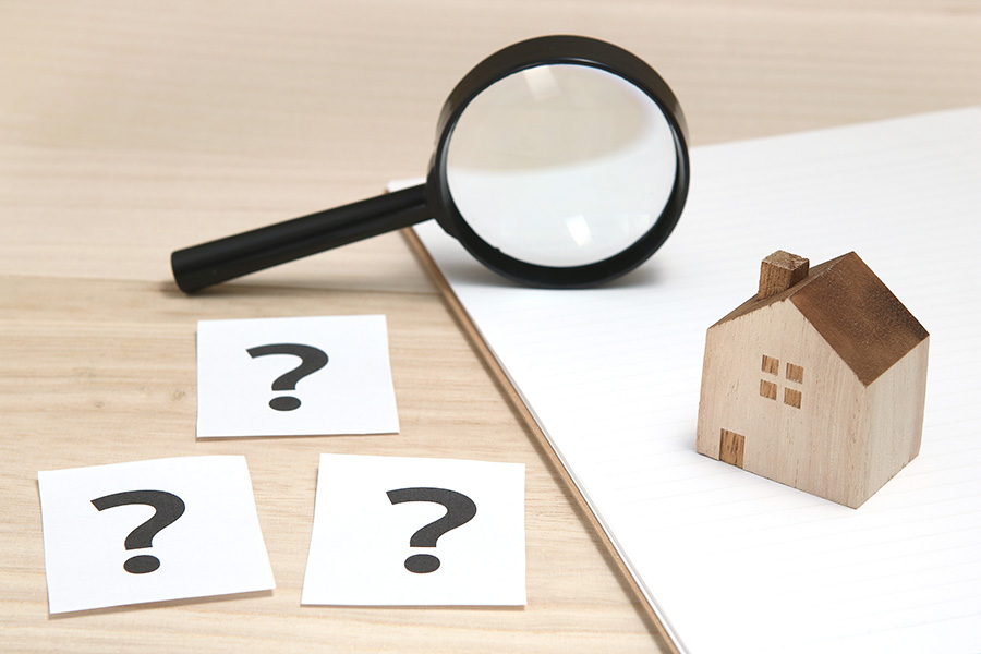 A small toy house next to a magnifying glass with handwritten question marks on pieces of paper