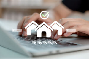 A close-up of hands on a keyboard overlaid with a graphic of simple white houses under a green tick mark