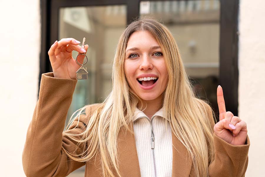 A young woman holds up a key on a keyring the shape of a house