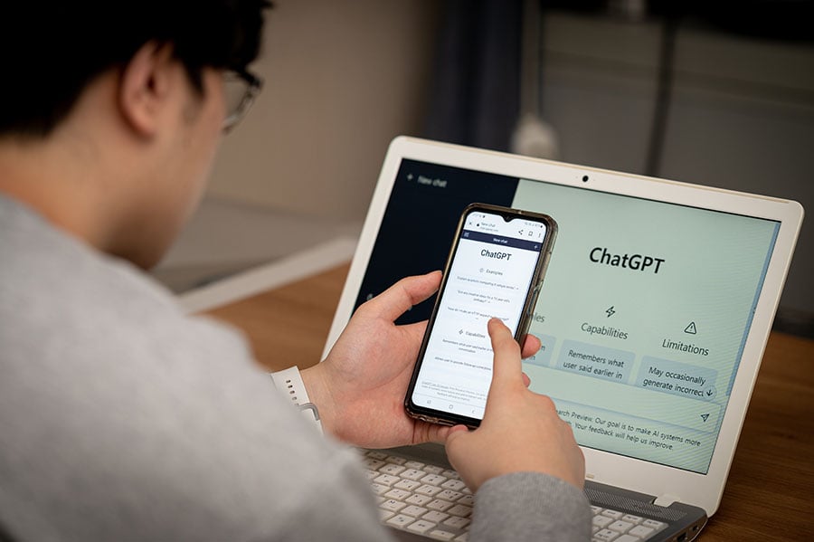 A man viewed from behind using chatgpt on his laptop and phone