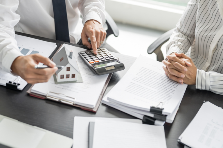 Close-up of hands using a calculator and looking at piles of paper