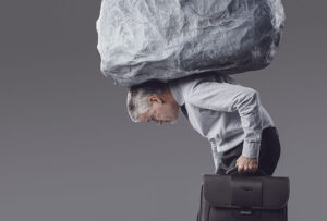 A man carrying a briefcase, bent over with a rock balanced on his back