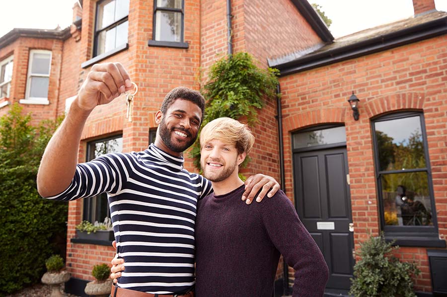 A smiling male couple hold up a set of house keys outside a house