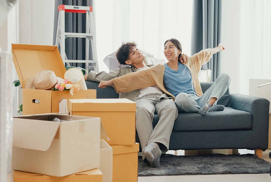 A smiling couple on a sofa surrounded by packing boxes