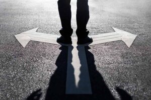 A close-up of a man standing on a crossroads, with arrows pointing left and right