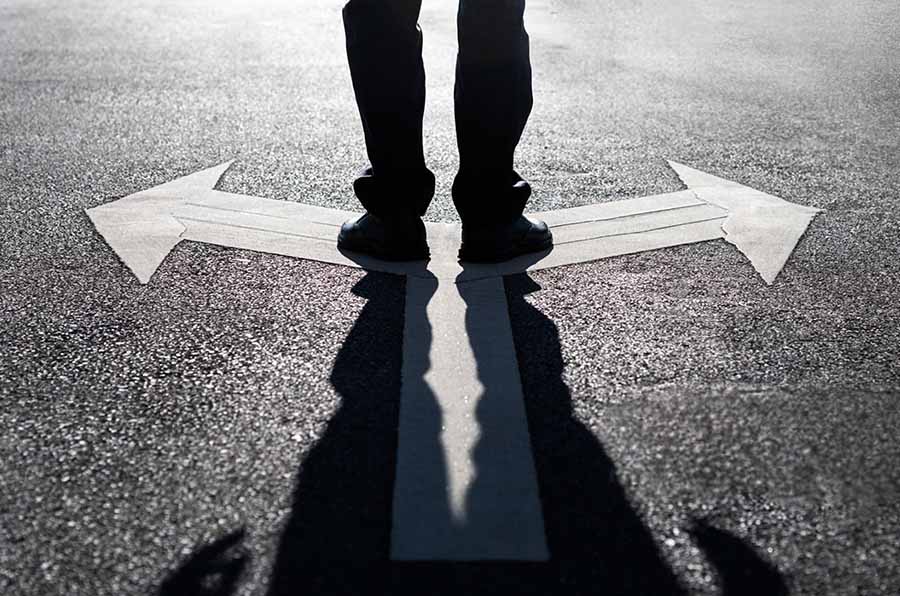 A close-up of a man standing on a crossroads, with arrows pointing left and right