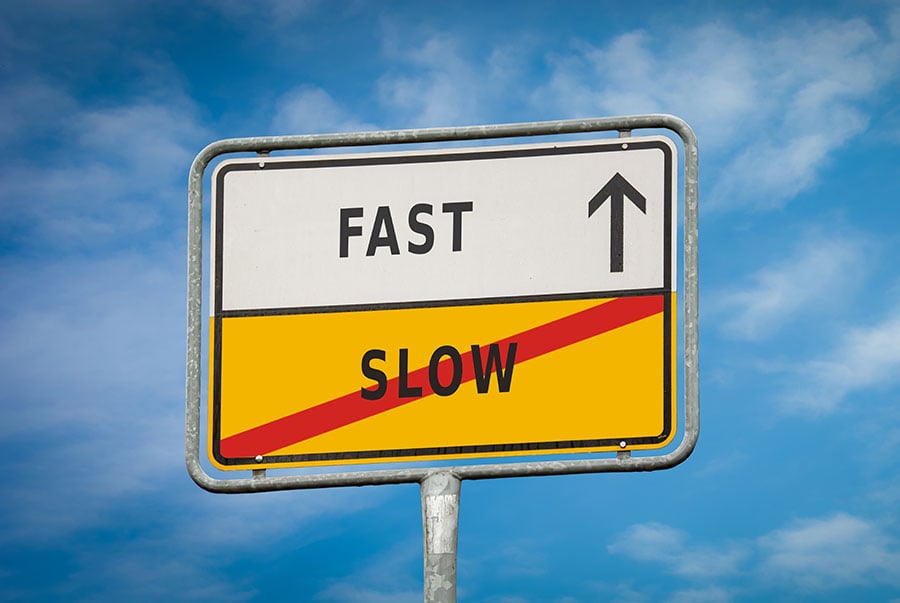 A sign with the words fast and slow, against a blue sky