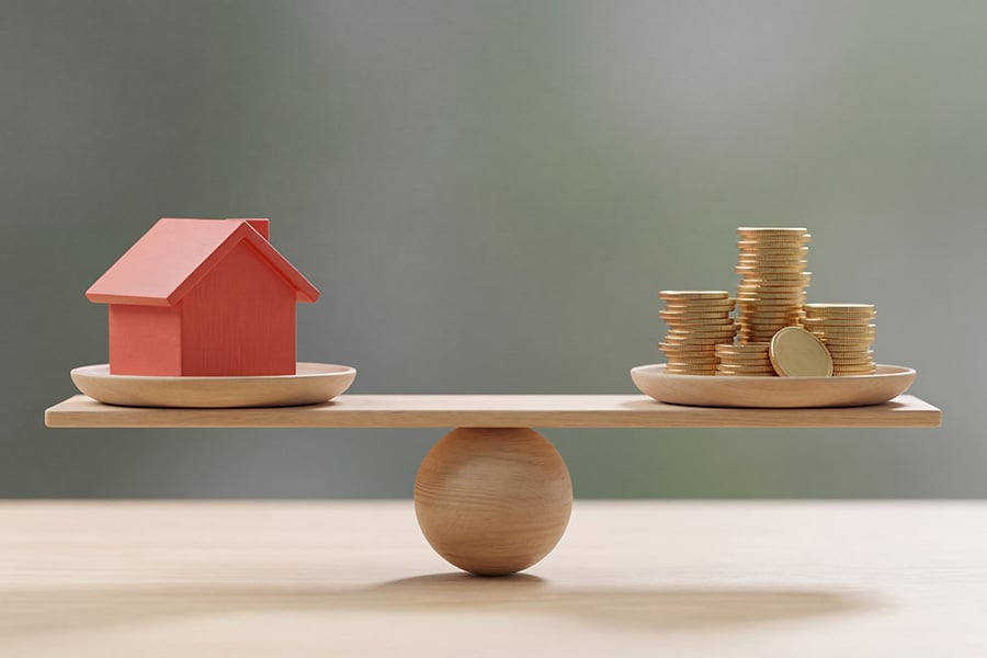 A balanced seesaw with a house on one side and coins on the other
