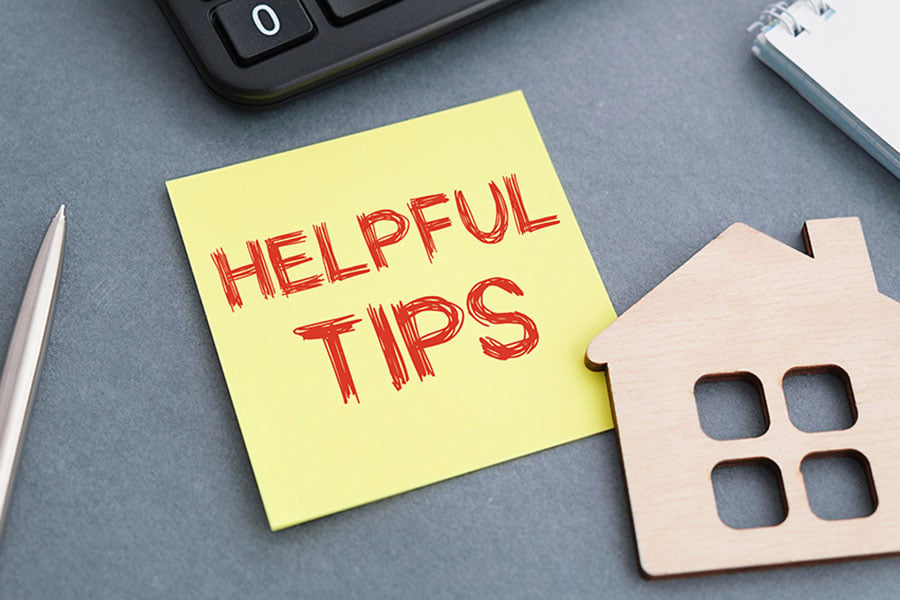 A desk arranged with a post-it with the words 'helpful tips', a pen, a keyboard, and a small wooden house shape