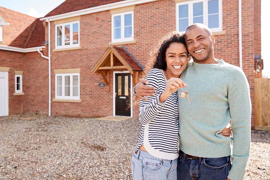 A smiling couple stand outside a large house holding up a set of keys