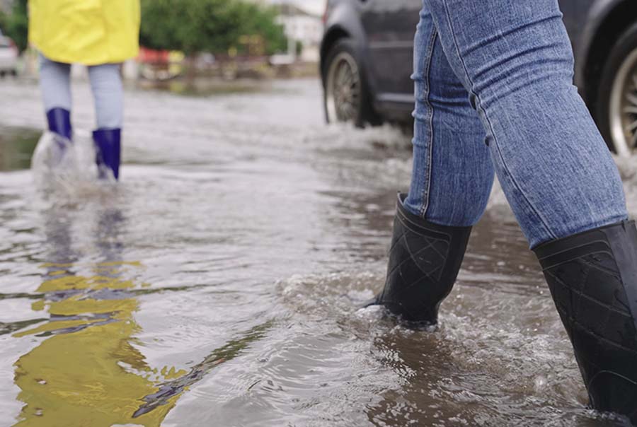 Two girls walk down a flooded street wearing raincoats and wellington boots