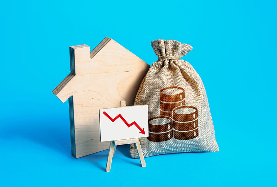 A small wooden house, a sack with a coin on the front and a graph with a downward-pointing arrow