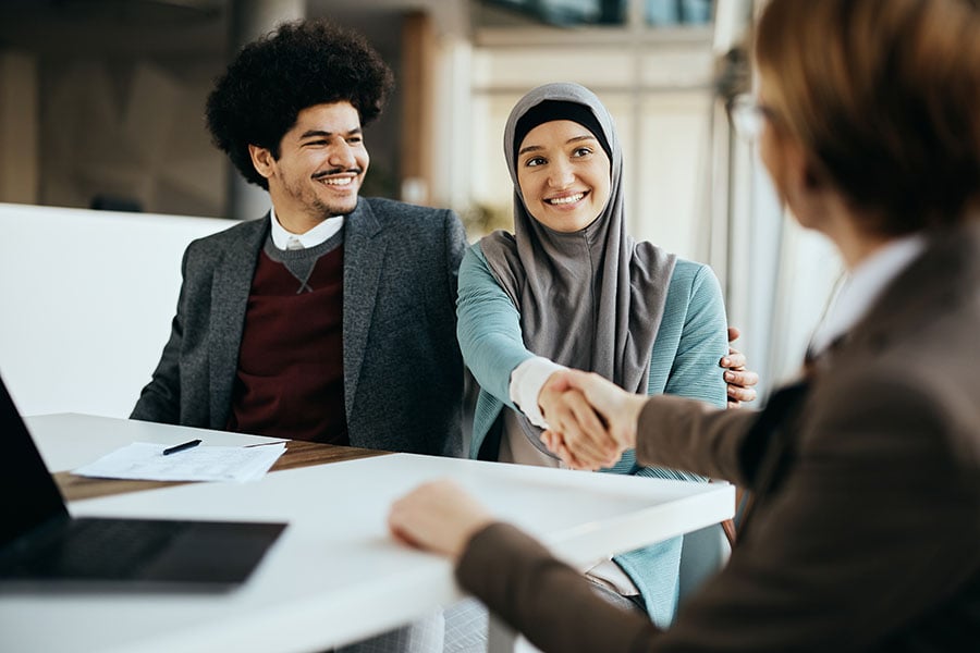 A happy muslim couple shake hands with a professional woman over a desk