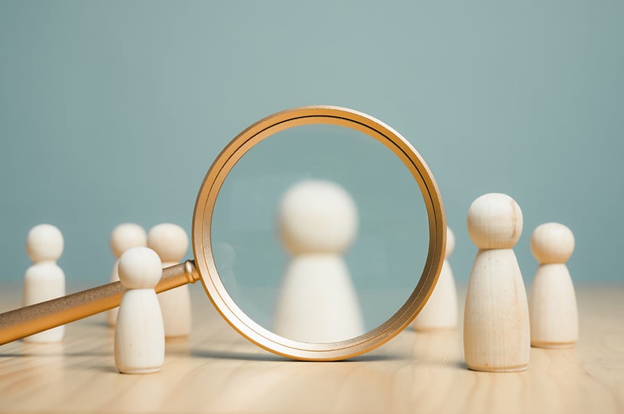 Small wooden figures with one highlighted by a magnifying glass