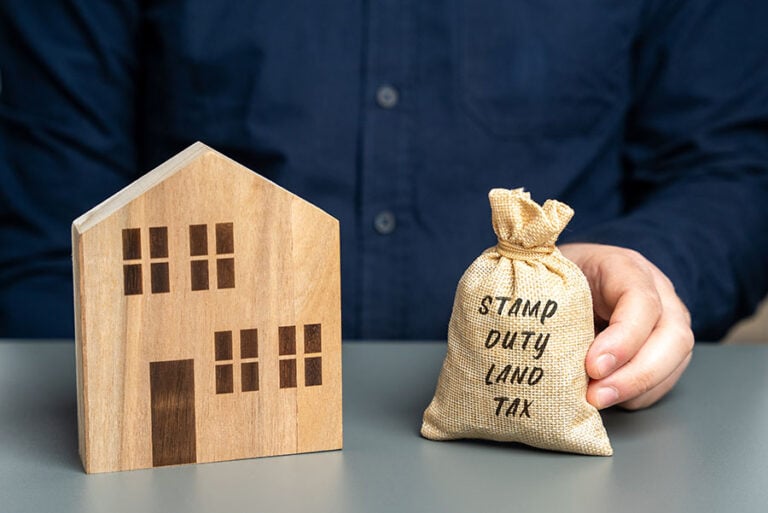 A sack marked 'stamp duty land tax' next to a small wooden house