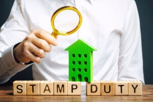 The words 'stamp duty' written in wooden blocks, with a man holding a magnifying glass over the top