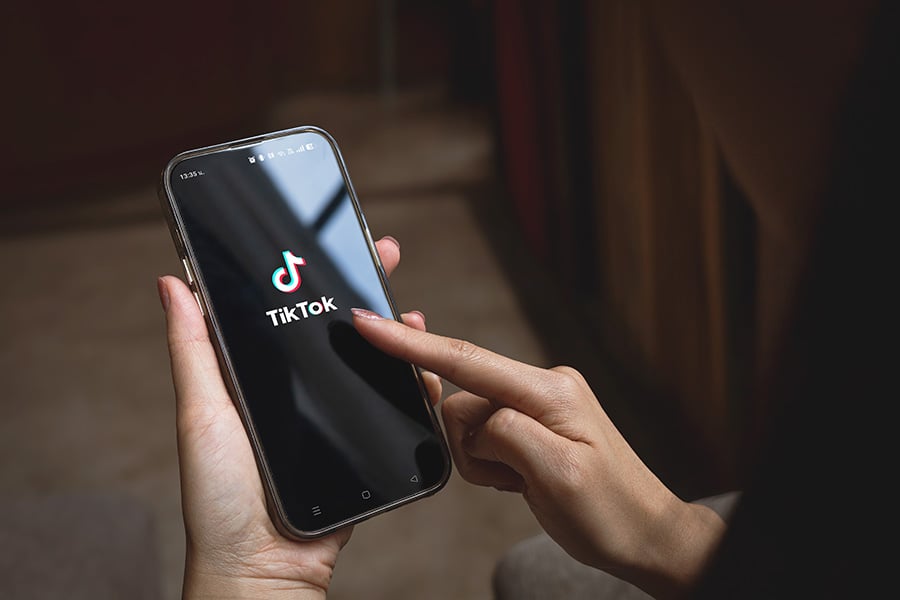 A close-up of a hand holding a phone with the TikTok app on the screen