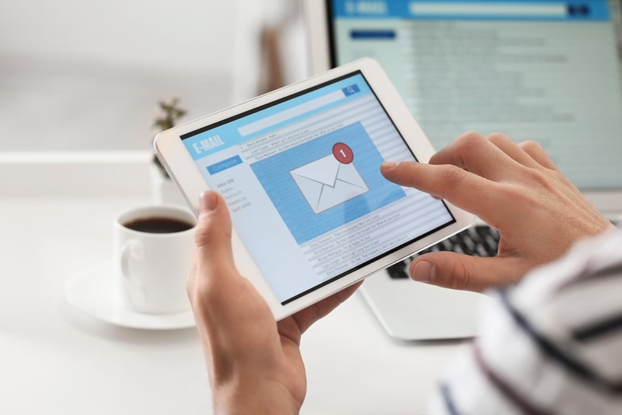 A hand holding a tablet which displays an email envelope on the screen