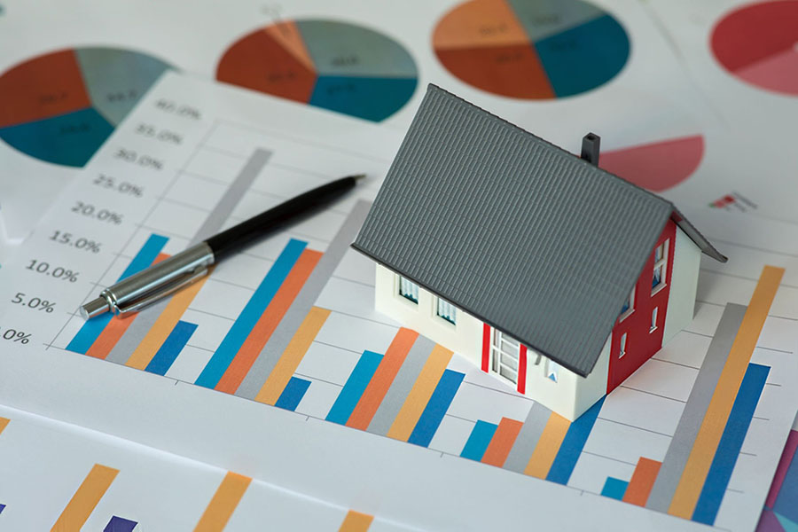 Colourful bar charts printed on white paper, with a small model of a house placed on the top