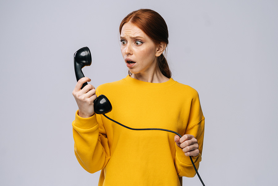 A shocked looking woman holds up an old-style telephone