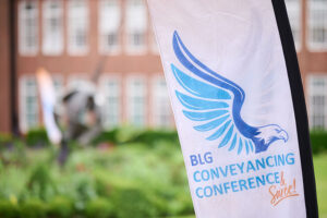 A flag in the foreground with the words BLG conveyancing conference, with a stately building and lawns in the background