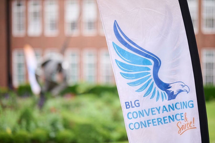 A flag in the foreground with the words BLG conveyancing conference, with a stately building and lawns in the background