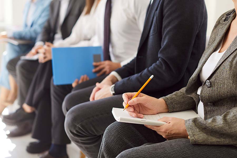 A group of professionals sitting in a row holding pens and notepads