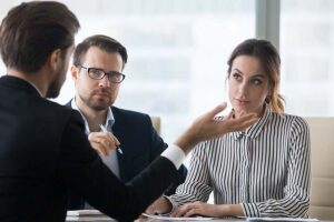 A lawyer seen from behind dressed in black suit gesticulates in front of a suspicious looking couple