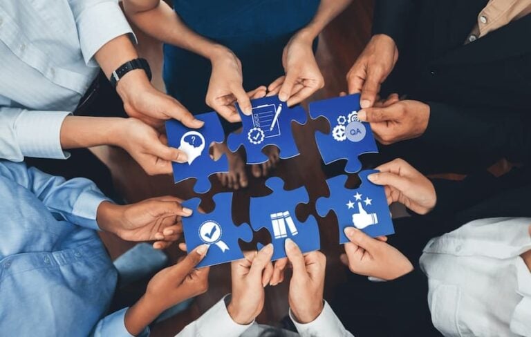 A diverse group of hands come together, holding blue puzzle pieces that symbolize collaboration