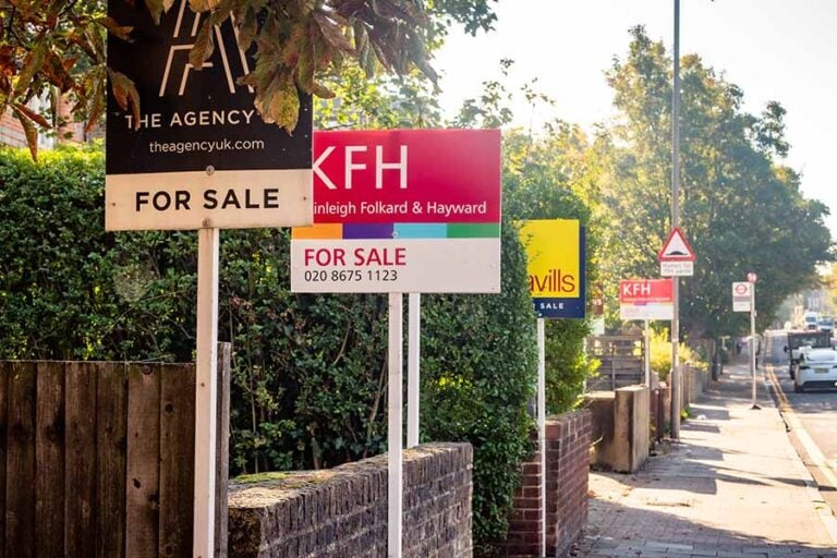 A row of for sale signs outside houses on a street in London