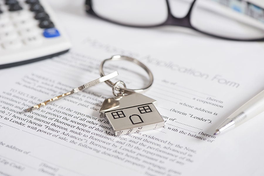 A house-shaped keyring on top of a mortgage application form and next to calculator