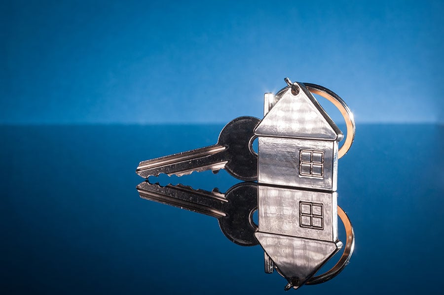 A silver key on a silver house keyring against a shiny blue background