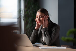 A tense-looking professional woman working at a laptop in an office
