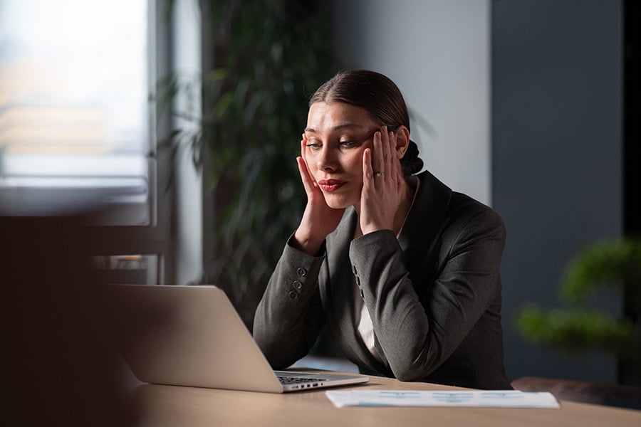 A tense-looking professional woman working at a laptop in an office