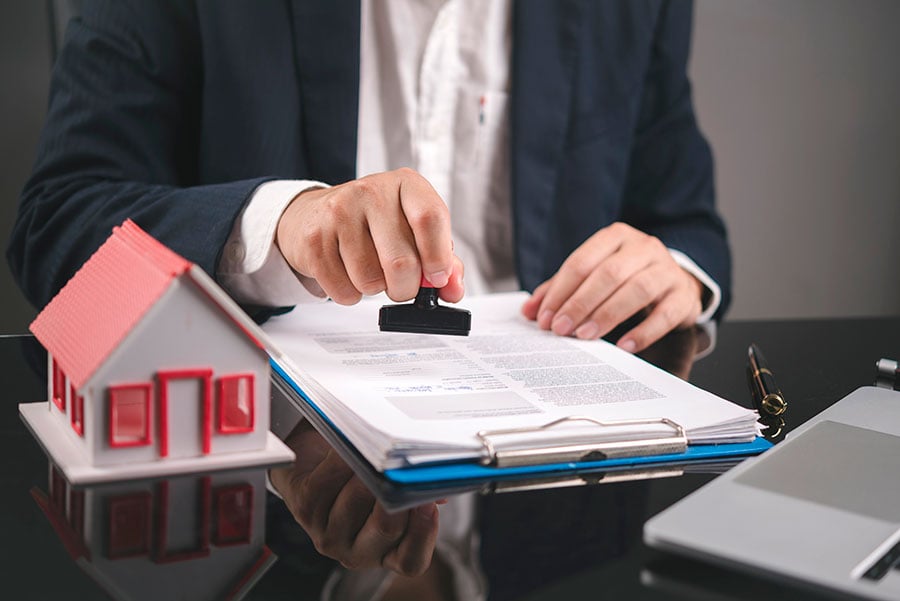 An estate agent stamps a pile of papers on a desk, next to a small model house