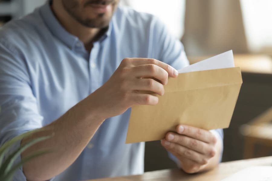 Close up young man opening envelope with paper correspondence.