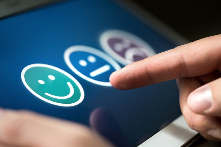 A finger points to three smiley faces on a screen to indicate levels of customer satisfaction