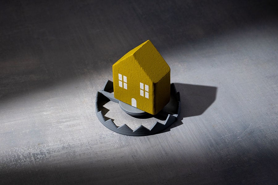 A toy yellow house in the middle of a bear trap against a shadowy background