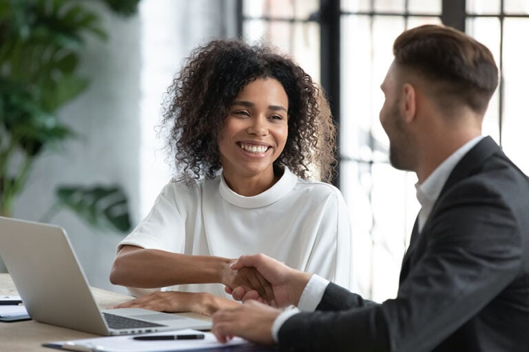 A happy looking woman shakes the hand of a man in a suit