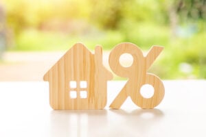 A small wooden house next to a percent symbol with a sunny green garden in the background