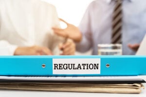 A file marked regulation in the foreground with two smartly dressed people in the background