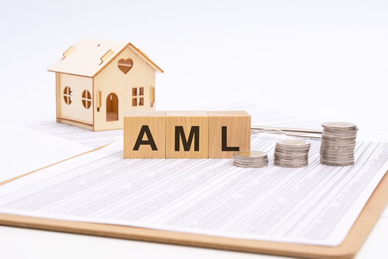 The letters AML on small wooden blocks, next to three piles of coins and in front of a small model of a house