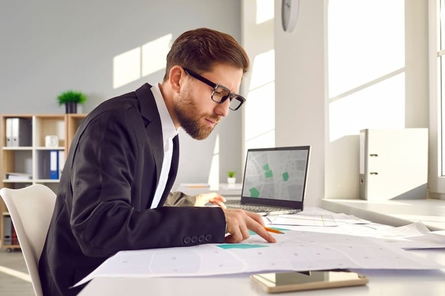 Professional surveyor in suit and glasses sitting at his table in office