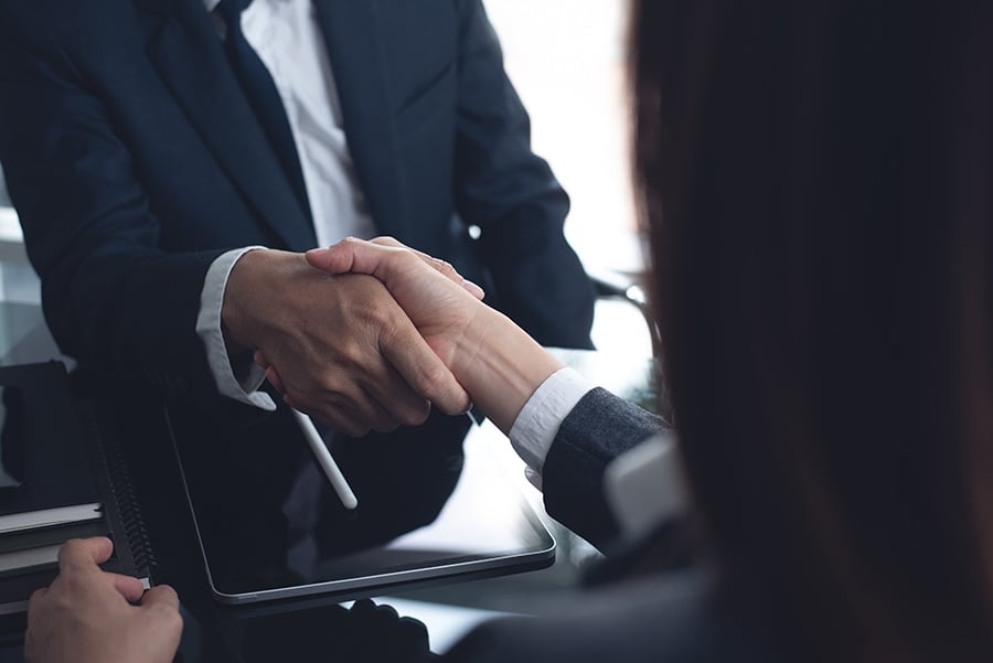 Close up of a handshake between a man and woman wearing black suits