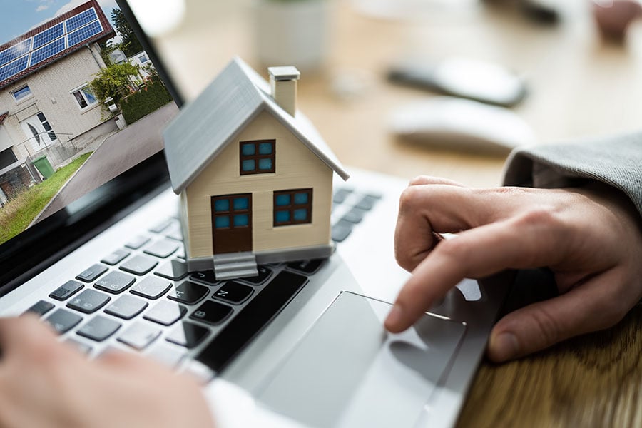 Close-up of hands on a laptop which has a picture of a house on the screen and a small toy house placed on the keyboard