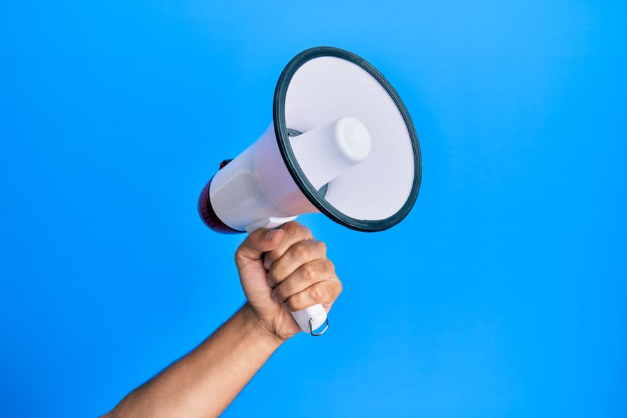 Hand of man holding megaphone over isolated blue background.