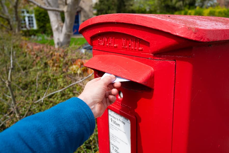 Person seen posting a letter in an old style, red-painted Royal Mail letter box.